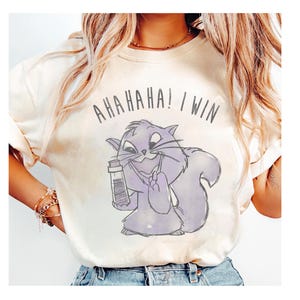 Puede incluir: Camiseta color crema con un dibujo de ardilla morada sosteniendo un vial. El texto "AHAHAHA! I WIN" está impreso encima de la ardilla. La camiseta tiene un corte holgado y mangas enrolladas.
