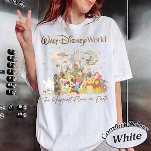 K&ouml;nnte beinhalten: Wei&szlig;es T-Shirt mit einem Disney-Motiv. Das Design zeigt die Schriftz&uuml;ge "Walt Disney World" und "The Happiest Place on Earth" sowie Illustrationen von Disney-Figuren und einem Schloss.