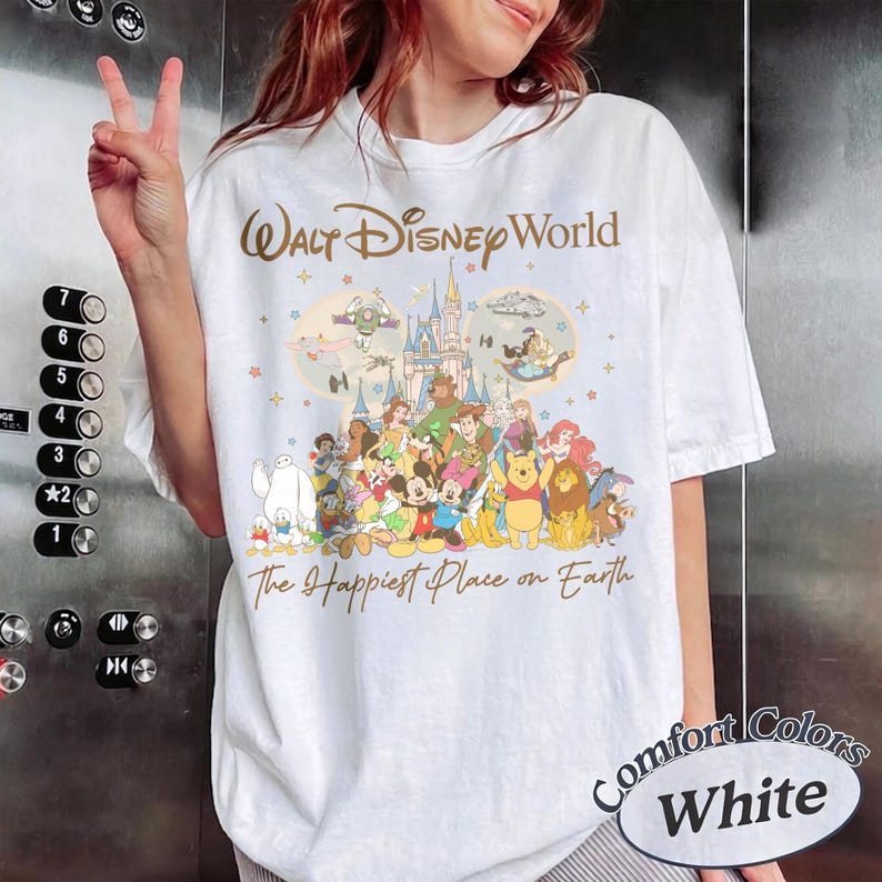 K&ouml;nnte beinhalten: Wei&szlig;es T-Shirt mit einem Disney-Motiv. Das Design zeigt die Schriftz&uuml;ge "Walt Disney World" und "The Happiest Place on Earth" sowie Illustrationen von Disney-Figuren und einem Schloss.