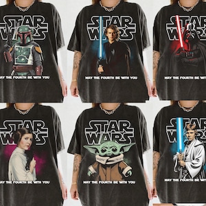 May include: Six dark grey t-shirts featuring Star Wars characters: Boba Fett, Anakin Skywalker, Darth Vader, Princess Leia, Grogu (Baby Yoda), and Luke Skywalker. Each shirt has the Star Wars logo and the phrase "May the Fourth Be With You."