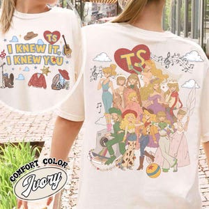 以下が含まれることがあります： アイボリー色のTシャツにグラフィックプリントが施されています。前面には「I KNEW IT, I KNEW YOU」の文字と、帽子、ハート、ギター、カーディガン、ブーツのアイコンが描かれています。背面には、複数のアニメキャラクターとハートの大きなイラストが描かれています。