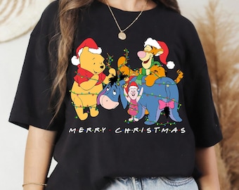 May include: Black t-shirt featuring Winnie the Pooh, Tigger, Eeyore, and Piglet wearing Santa hats and Christmas lights. The words "MERRY CHRISTMAS" are printed across the bottom in red.