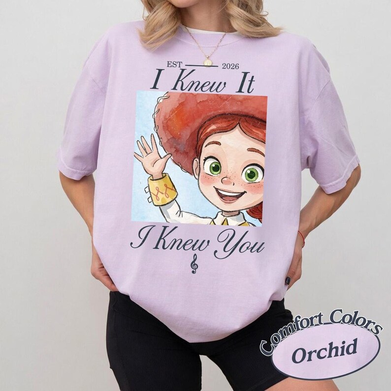 Peut inclure: Un t-shirt &agrave; manches courtes violet clair avec une illustration d'un personnage aux cheveux roux portant un chapeau rouge. Le texte indique EST 2026, I Knew It, et I Knew You, avec une note de musique en dessous. Col rond classique.