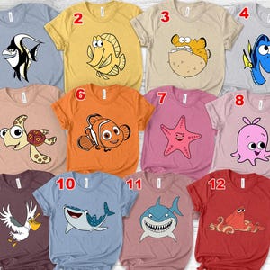 Può includere: Magliette assortite con creature marine dei cartoni animati. I disegni includono un pesce bianco e nero, un pesce giallo, un pesce palla, un pesce blu, una tartaruga, un pesce pagliaccio arancione, una stella marina rosa, un polpo rosa, un pellicano, uno squalo balena, uno squalo e un granchio rosso.