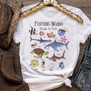 May include: White t-shirt with a Finding Nemo Guide to Fish graphic. The graphic features various characters from the movie, including Nemo, Dory, Marlin, and Gill. Each character is labeled with their name.