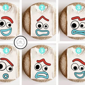 May include: Six cream-colored t-shirts with different cartoon face designs. Each shirt features a red eyebrow, black eyes, and a blue mouth. The shirts are arranged on woven mats, with a circular logo in the center.