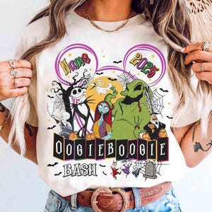 Puede incluir: Camiseta color crema con un diseño gráfico colorido con personajes de Pesadilla antes de Navidad. El diseño incluye a Jack Skellington, Sally, Oogie Boogie y el texto "Oogie Boogie Bash" y "2023".
