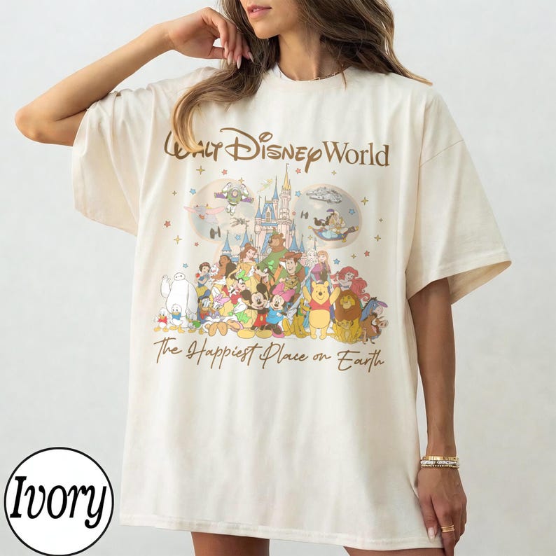 May include: Ivory-colored t-shirt featuring a graphic of Disney characters with the text "Walt Disney World" and "The Happiest Place on Earth". The design includes a castle, stars, and various cartoon characters.