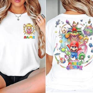 Pu&ograve; includere: T-shirt bianco con una grafica colorata di Princess Peach e la scritta "NAME" sul davanti. Il retro della maglietta mostra una vivace illustrazione dei personaggi del gioco "The Super Mario Galaxy".