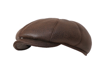 May include: A dark brown leather flat cap featuring a multi-panel construction with visible stitching and a short, curved brim. The textured surface of the leather shows natural grain patterns across the rounded crown of this classic headwear piece.