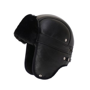 Pode incluir: Chap&eacute;u de aviador de couro preto com aba de orelha de pele e correia para o queixo. O chap&eacute;u tem fecho de fivela e um bot&atilde;o de metal prateado.