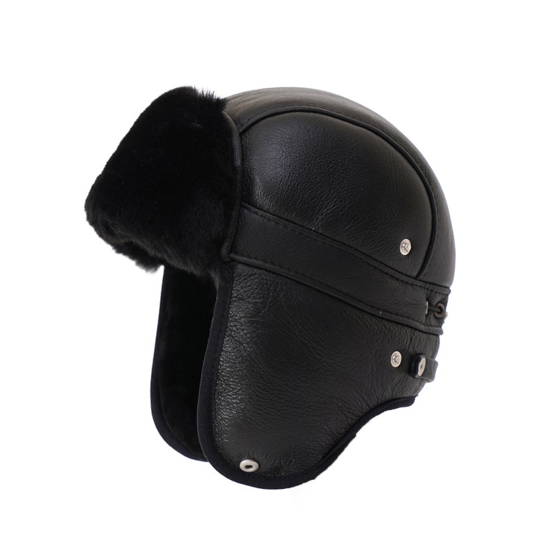 Pode incluir: Chap&eacute;u de aviador de couro preto com aba de orelha de pele e correia para o queixo. O chap&eacute;u tem fecho de fivela e um bot&atilde;o de metal prateado.