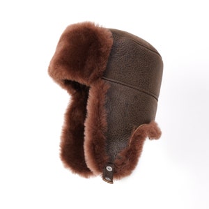 May include: A brown leather and fur aviator hat with ear flaps. The hat has a brown leather exterior and a brown fur lining. The ear flaps are made of fur and can be tied at the top of the hat.