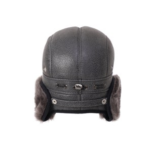 Pode incluir: Um chap&eacute;u de aviador de couro cinza com abas de orelha forradas de pele cinza. O chap&eacute;u tem uma correia com fivela e dois bot&otilde;es de metal de cada lado.