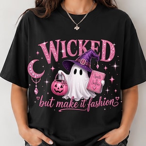 May include: A black t-shirt featuring a graphic of a white ghost wearing a purple witch hat. The ghost holds a pink jack-o'-lantern bucket and a pink book titled Spells & Selfies. The text WICKED but make it fashion is printed in pink glitter.