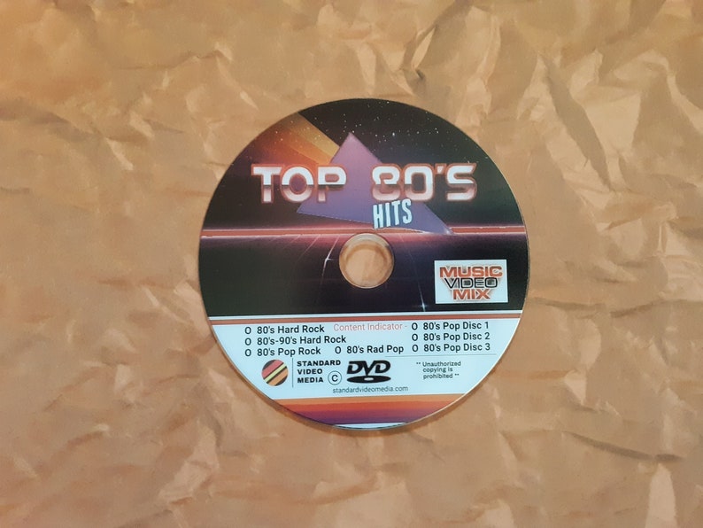 May include: A DVD disc labeled "Top 80's Hits Music Video Mix" with a black and red design. The disc includes 80's Hard Rock, 80's-90's Hard Rock, 80's Pop Rock, and 80's Rad Pop music videos.