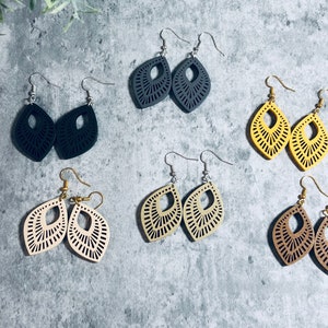 May include: Five pairs of dangle earrings with a geometric design. The earrings are made of wood and come in black, beige, brown, and yellow.