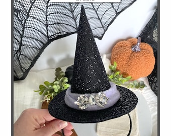 Puede incluir: Diadema de sombrero de bruja negro con una banda de terciopelo morado y adorno de pedrería. La diadema está decorada con purpurina negra. "Foxie Boutique Studio" está escrito en la imagen.