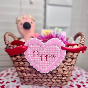 May include: A wicker basket with a pink and white gingham heart-shaped tag that says "Pippa". The basket is filled with gifts and a pink flamingo plush toy.