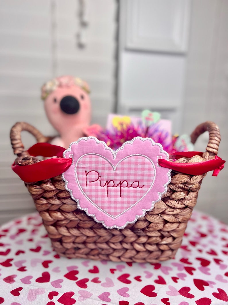 May include: A wicker basket with a pink and white gingham heart-shaped tag that says "Pippa". The basket is filled with gifts and a pink flamingo plush toy.