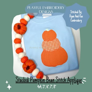 Op de afbeelding: Een lichtblauw shirt met lange mouwen met een oranje gestapelde pompoen applicatie. Het shirt is versierd met een vilten slinger van oranje en witte pompoenen. Tekst op de afbeelding luidt "Playful Embroidery Designs" en "Stacked Pumpkin Bean Stitch Applique".