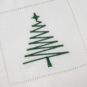 May include: White linen napkin with a green embroidered Christmas tree design.