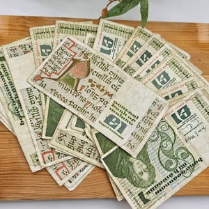 Peut inclure: Une collection de billets de banque de style ancien, avec une calligraphie et des illustrations complexes à l'encre verte, rouge et noire. Les billets sont disposés sur une surface en bois, mettant en valeur une esthétique vintage. Le texte comprend les mots "General Bank of Ireland".