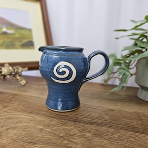 Può includere: Una lattiera in ceramica blu fatta a mano con un disegno a spirale bianco. La lattiera ha un manico e un beccuccio per versare facilmente. La lattiera è alta circa 10 cm ed è un'aggiunta unica a qualsiasi cucina.