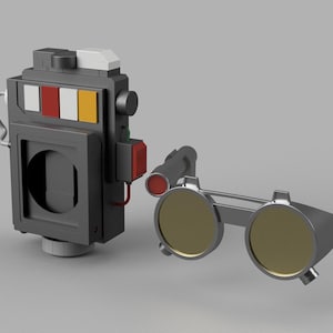 Può includere: Un dispositivo grigio rettangolare con un'apertura circolare e un paio di occhiali rotondi e colorati. Il dispositivo ha una serie di luci rettangolari colorate: bianco, rosso, bianco e giallo. Gli occhiali hanno una montatura argentata e lenti gialle.