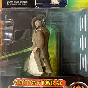 May include: A Star Wars action figure of Ben (Obi-Wan) Kenobi from the Rebel Alliance. The figure has a brown robe and a lightsaber that glows. The packaging says "Electronic Power F/X" and "With glowing lightsaber and remote dueling action".