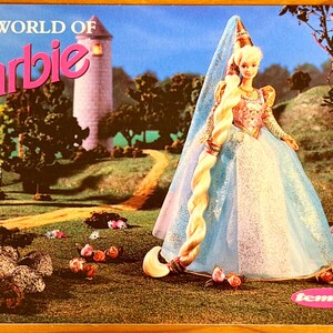 May include: A vintage Barbie doll in a long blue and pink gown with a long blonde braid. The doll is set against a backdrop of a castle, trees, and a path. The words "THE WORLD OF Barbie" are displayed in pink.