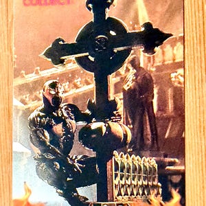May include: A collectible card featuring a detailed illustration of the Spawn character kneeling before a large cross. The card has a fiery background with the word "SPAWN" at the bottom and the word "COLLECT!" at the top.