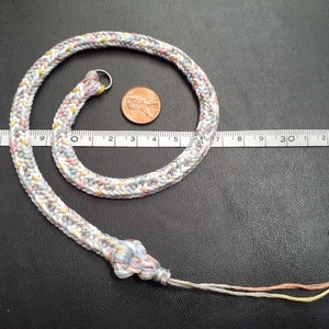 May include: A multi-colored braided cord necklace with a silver clasp. The cord is approximately 15 inches long and is made of a variety of colors, including pink, blue, white, and yellow.