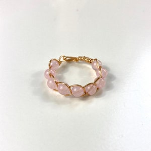 Könnte beinhalten: Ein Ring aus Golddraht mit rosafarbenen Rosenquarzperlen. Der Ring ist mit einem einfachen Drahtdesign gefertigt und verfügt über einen Cluster aus Rosenquarzperlen.