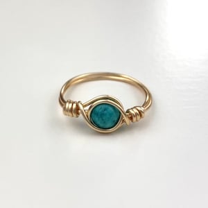 Könnte beinhalten: Ein goldfarbener Ring mit einem türkisfarbenen Stein, der mit Draht umwickelt ist.