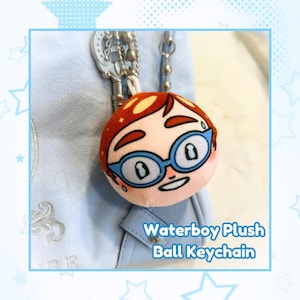 May include: A plush ball keychain featuring a cartoon face with red hair, blue glasses, and a smiling expression. The keychain is attached to a light blue bag. Text on the image reads "Waterboy Plush Ball Keychain."