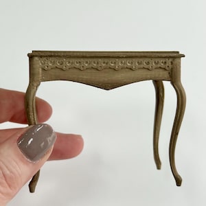 May include: A small, wooden table with a carved, ornate top and curved legs. The table is painted a light brown colour.