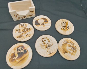 May include: Set of six wooden coasters featuring horror movie characters. The coasters are round and have a light brown wood finish. The characters include Jason Voorhees, Freddy Krueger, Michael Myers, Ghostface, and Pennywise. The coasters come with a wooden holder that says "Do you like scary movies?"