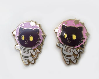 Puede incluir: Dos pines de esmalte dorado con un gato negro que lleva un traje de astronauta con un fondo espacial rosa y blanco. El texto "BBT" está en el traje.