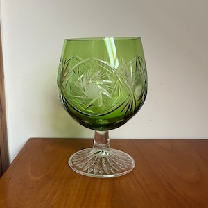 Op de afbeelding: Een groene glazen kelk met een geslepen glasontwerp. De kelk heeft een heldere steel en een heldere basis.
