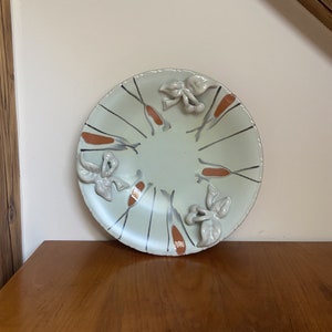 Puede incluir: Un plato redondo de cerámica con un esmalte verde claro y detalles marrones. El plato tiene un diseño en relieve de hojas y bayas alrededor del borde.