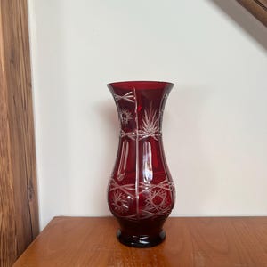 Op de afbeelding: Een rode glazen vaas met een geslepen glasontwerp. De vaas heeft een brede opening en een smalle basis.