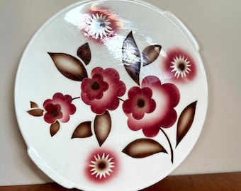 Op de afbeelding: Een wit keramiek bord met een bloemenmotief. De bloemen zijn rood, roze en bruin. Het bord heeft een gegolfde rand.