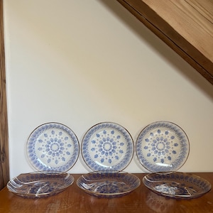 Könnte beinhalten: Satz von sechs Glastellern mit einem blauen und goldenen Blumenmuster. Die Teller sind in zwei Reihen zu je drei angeordnet. Die Teller befinden sich auf einer Holzoberfläche.