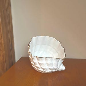 Op de afbeelding: Witte keramische schelpvormige plantenpot met een gouden rand. De pot is getextureerd.