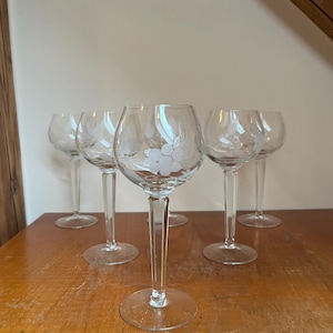 May include: Set of six clear glass wine glasses with etched grape designs. The glasses have a round bowl and a long stem.