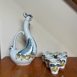 Peut inclure: Une carafe en porcelaine blanche en forme de paon avec des accents bleus et dorés, et six verres à liqueur assortis avec un design similaire.