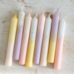 Könnte beinhalten: Ein Set aus acht Ombre-Kerzen mit einem Farbverlauf von hellrosa, gelb und weiß. Die Kerzen haben eine gesprenkelte Glitzer-Oberfläche.