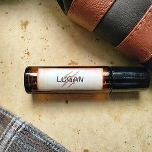May include: A brown glass roller bottle with a white label that says "LOGAN" with a red claw mark design.