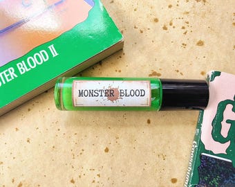 May include: A green glass roller bottle with a black cap. The label reads "MONSTER BLOOD" in white text with a brown splatter design.